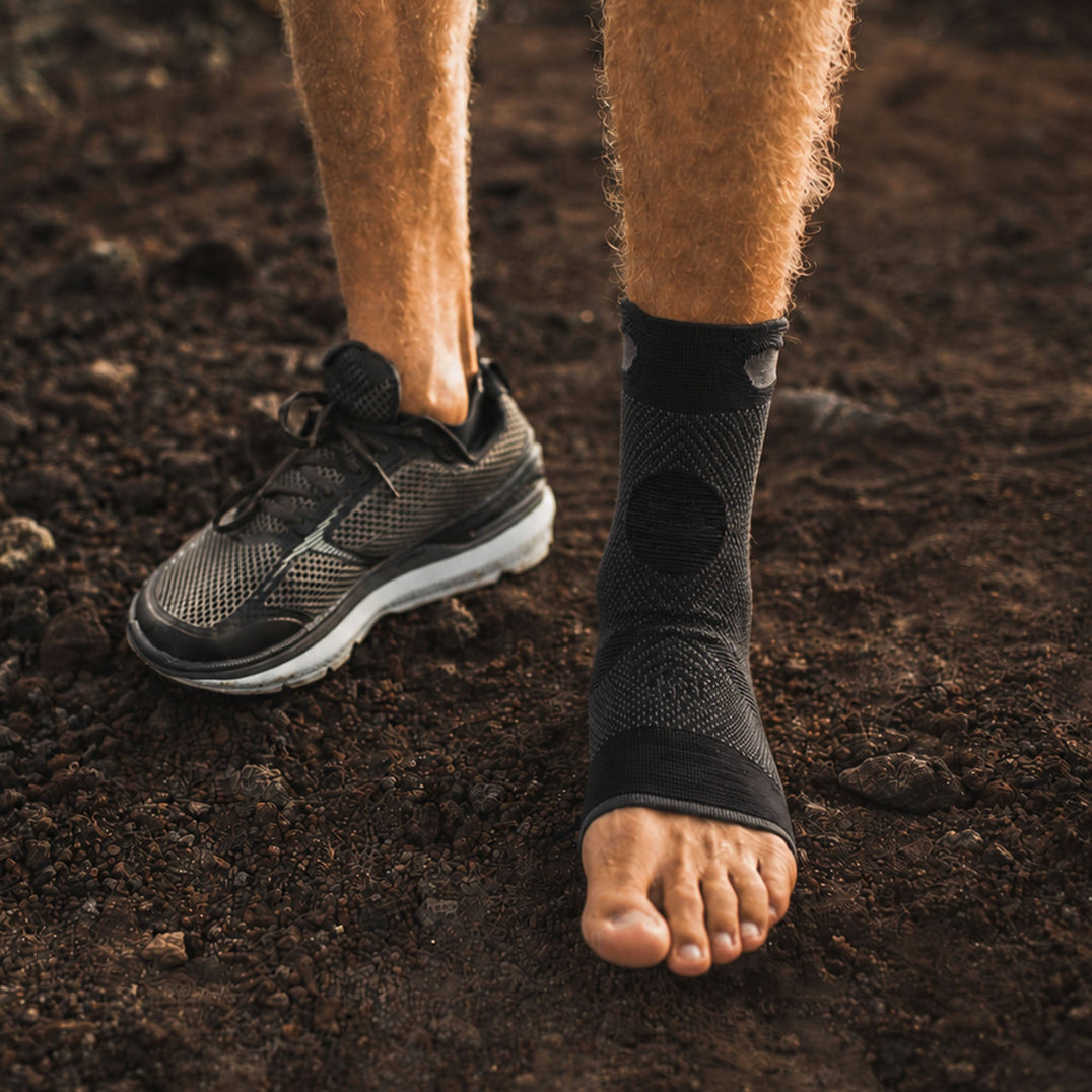 Homme se tenant debout portant un chaussure au pied droit et une chevillère de compression au pied gauche