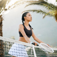 Joueuse de tennis s'appuyant sur le filet de tennis avec sa raquette dans les mains